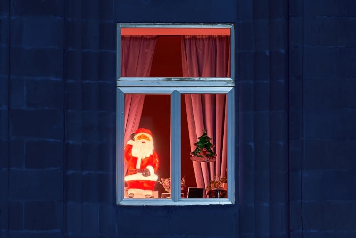 Widok na świąteczne okno w którym stoi świecąca dekoracja w kształcie Świętego Mikołaja